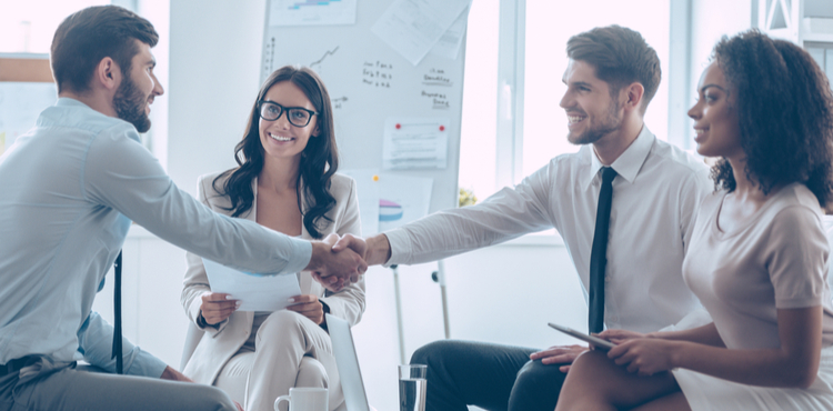 Men shaking hands in an office amongst a group. Men shaking hands in an office amongst a group.