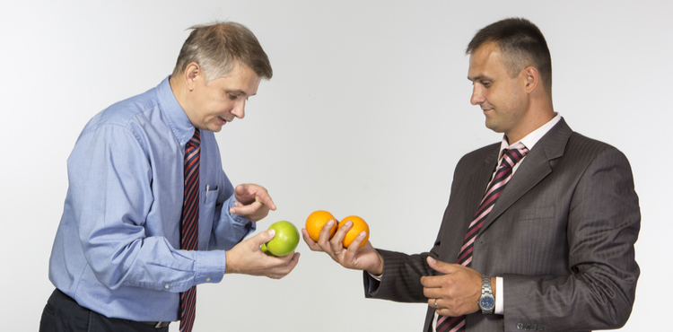 Two men in suits compare apples and oranges. Two men in suits compare apples and oranges.