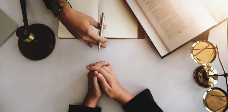 A view of a desk from above with hands, papers, a gavel, and scales. A view of a desk from above with hands, papers, a gavel, and scales.