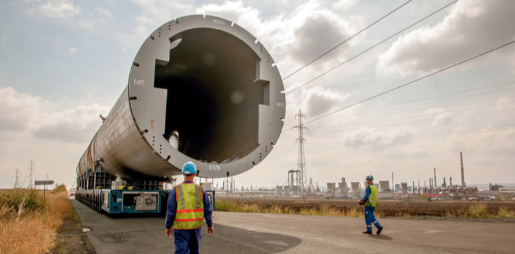 A worker walks toward a large pipe used for transporting oil. A worker walks toward a large pipe used for transporting oil.