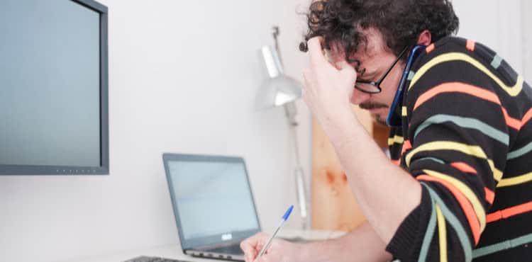 Man at desk writing while on phone Man at desk writing while on phone