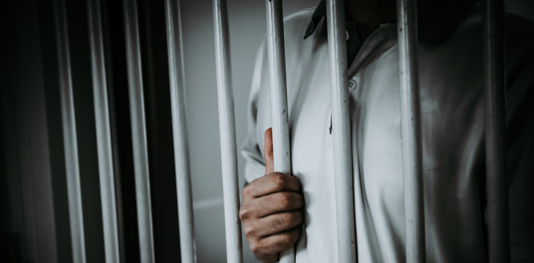 Man standing behind bars in jail cell. Man standing behind bars in jail cell.