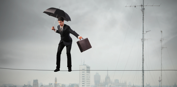 Man balancing on a tightrope with an umbrella and a briefcase.