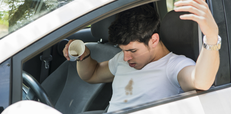 A man in a car spills coffee on himself. A man in a car spills coffee on himself.
