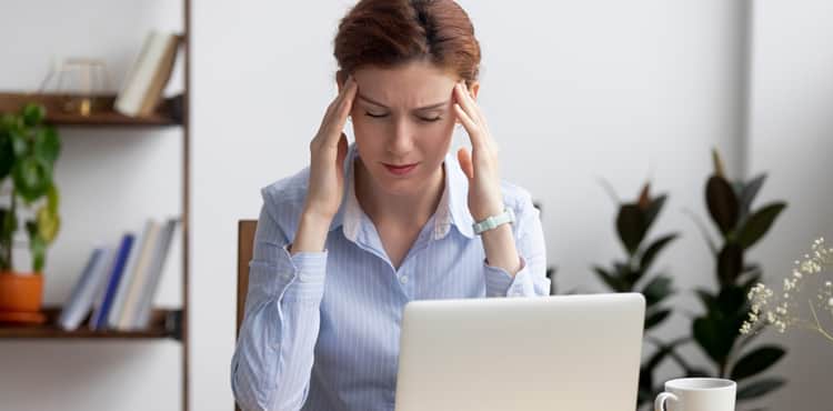 Woman at laptop holds her temples. Woman at laptop holds her temples.