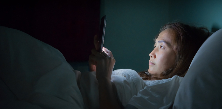 A woman scrolls through her phone in bed at night. A woman scrolls through her phone in bed at night.