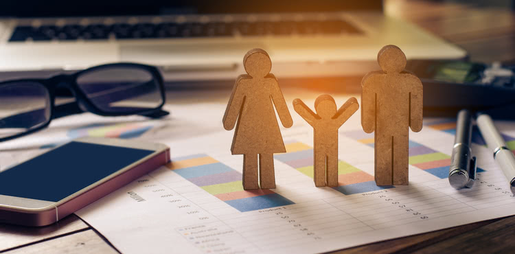 A wooden block family standing on paperwork on a desk. A wooden block family standing on paperwork on a desk.