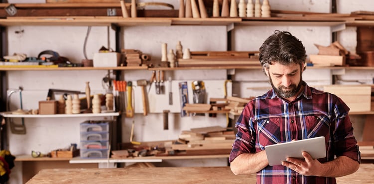 A man on an iPad standing in a woodworking shop. A man on an iPad standing in a woodworking shop.
