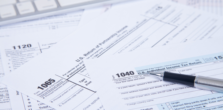 Tax forms strewn across a table with a pen. Tax forms strewn across a table with a pen.