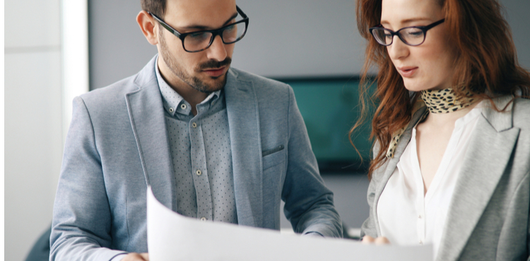 A woman and a man standing and reviewing a paper document. A woman and a man standing and reviewing a paper document.