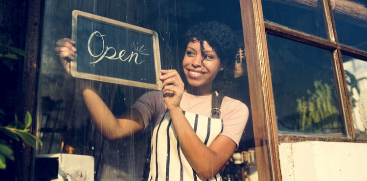 A woman holding an open sign wearing an apron. A woman holding an open sign wearing an apron.