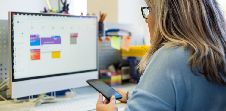 Woman working at computer with phone in hand. Woman working at computer with phone in hand.