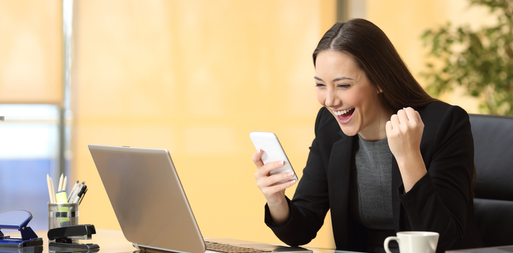 A woman sitting at her desk laughing at her phone. A woman sitting at her desk laughing at her phone.