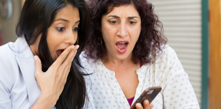 Two women are shocked by what they see on a phone.