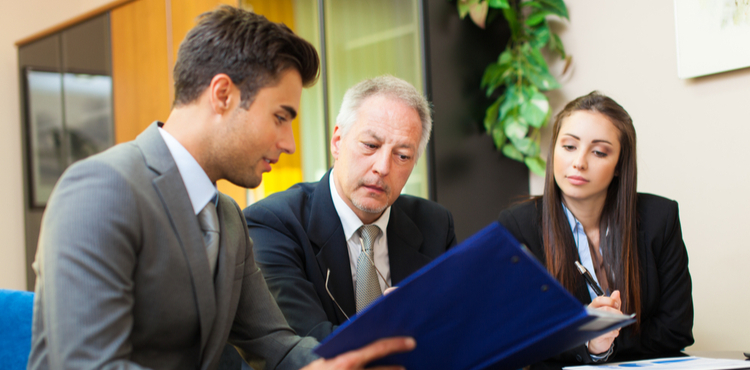 Three business people look through a binder. Three business people look through a binder.