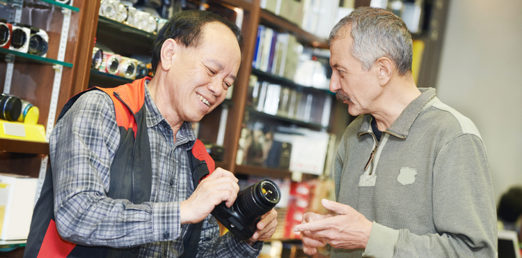 A salesperson shows a customer a camera in a small camera store.