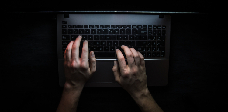 A laptop computer barely illuminated and someone typing. A laptop computer barely illuminated and someone typing.