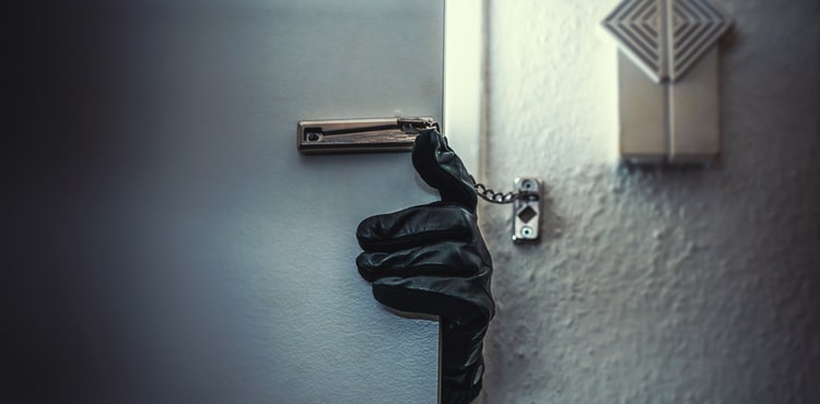 A gloved burglar's hand opening a locked door.