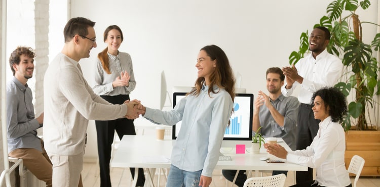 A business man and woman shake hands during a meeting with staff.