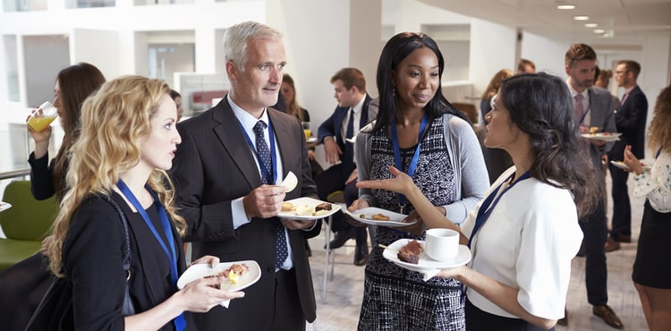 A group of people standing with food at a business event. A group of people standing with food at a business event.