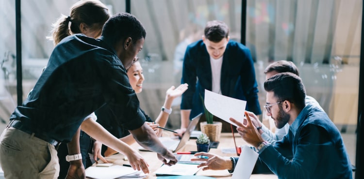 A group of people stand or sit around a conference table. A group of people stand or sit around a conference table.