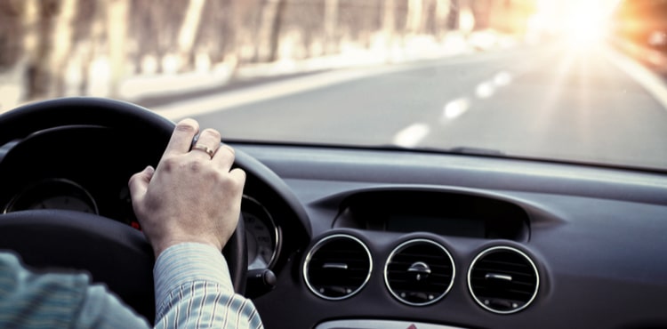 A man's hand on the steering wheel of a car driving down a road. A man's hand on the steering wheel of a car driving down a road.