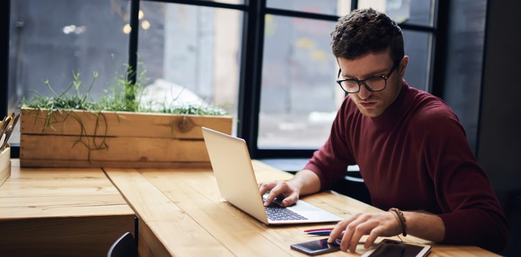 A man looking at his phone and working on a laptop. A man looking at his phone and working on a laptop.