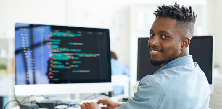 A man looking at the camera smiling in front of a computer. A man looking at the camera smiling in front of a computer.