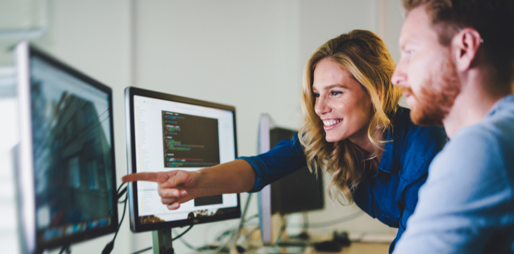 A woman points and smiles at a computer screen. A woman points and smiles at a computer screen.