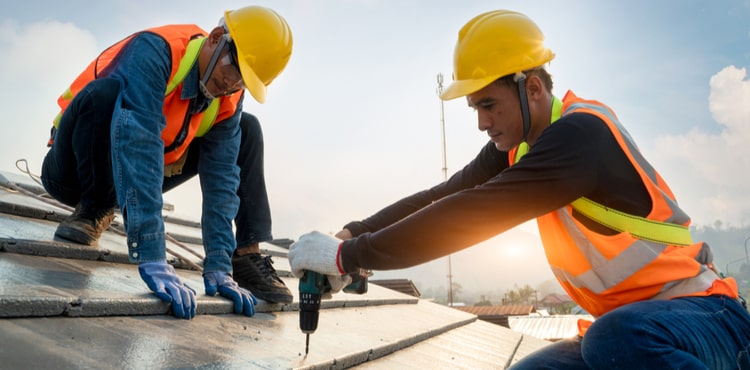 Two people in helmets working on a roof.