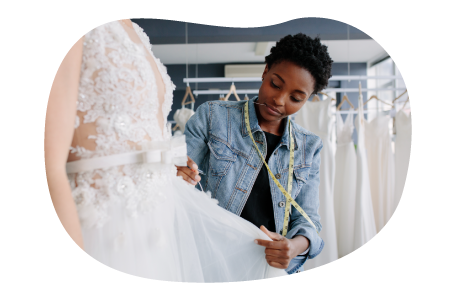 Bridal shop employee measuring a client wearing a wedding dress.