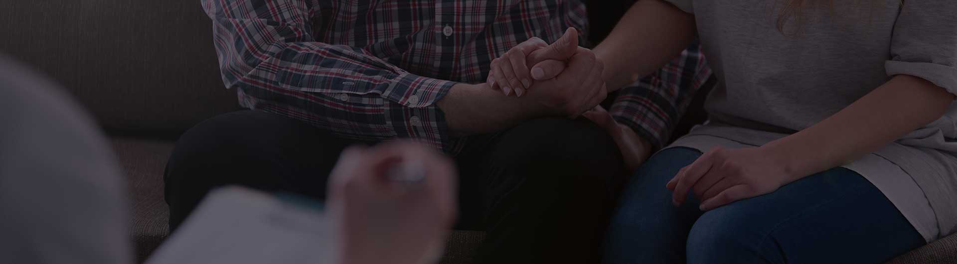 Woman and man holding hands on a couch during a therapy session.