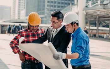 Contractors and a businessman review building plans.