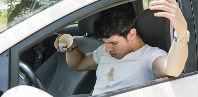 A man in a car spills coffee on himself.