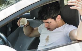 A man in a car spills coffee on himself.