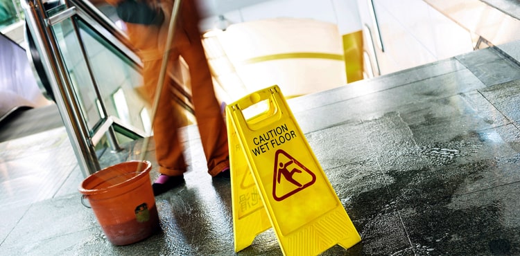 A person mops in front of a caution wet floor sign.