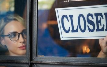 Woman puts closed sign in window of business.