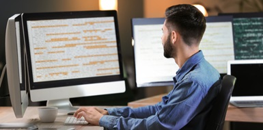 A lone computer programmer works on multiple screens in an office.