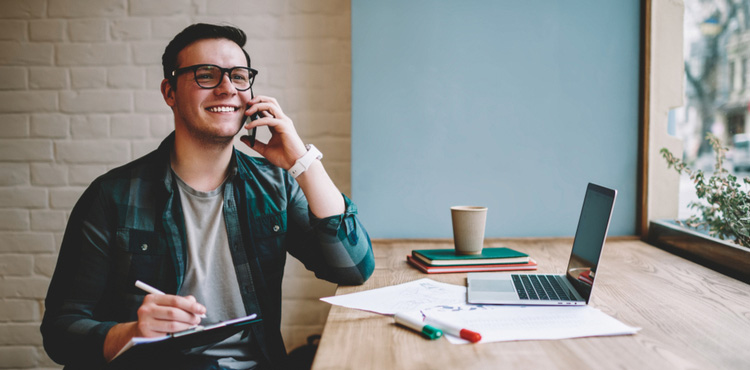 Freelancer on the phone taking notes in front of his laptop.