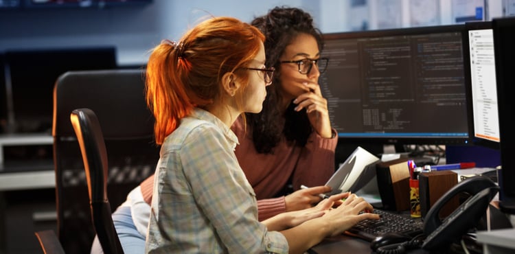 Two women examine code together on a computer display. Two women examine code together on a computer display.