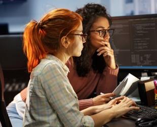 Two women examine code together on a computer display.