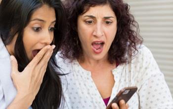 Two women are shocked by what they see on a phone.