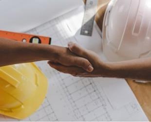 Two construction contractors shake hands over building plan.