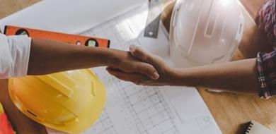 Two construction contractors shake hands over building plan.