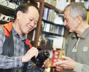 A salesperson shows a customer a camera in a small camera store.