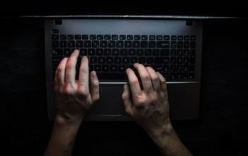 A laptop computer barely illuminated and someone typing.