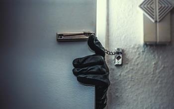 A gloved burglar's hand opening a locked door.