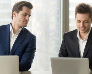 A man glancing at another man's laptop screen.