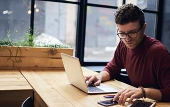 A man looking at his phone and working on a laptop.