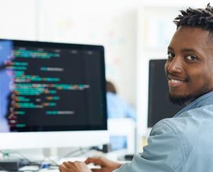 A man looking at the camera smiling in front of a computer.